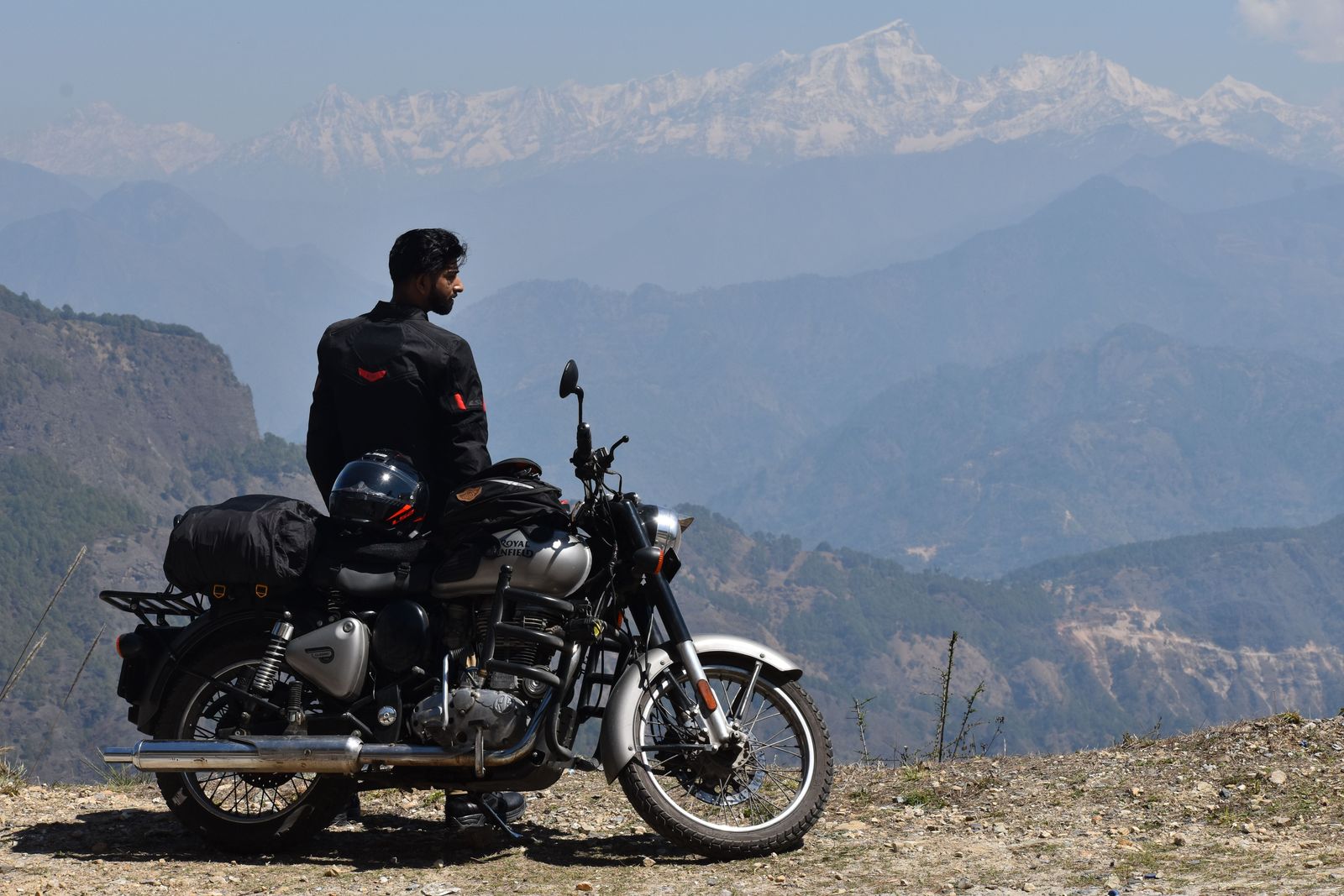 Motero con casco junto a su Royal Enfield mirando la cordillera